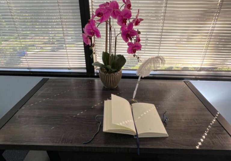 Open book and pink orchids on a rustic wooden table by a window.